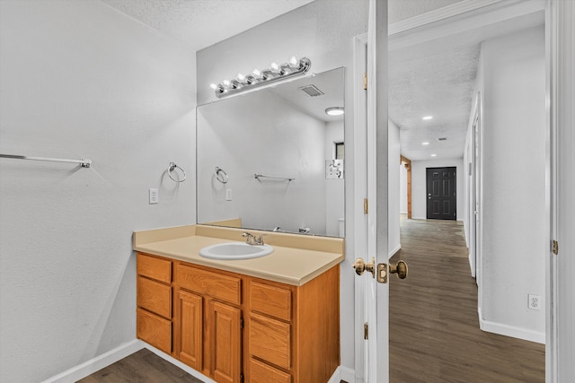 bathroom with a textured ceiling, baseboards, wood finished floors, and vanity