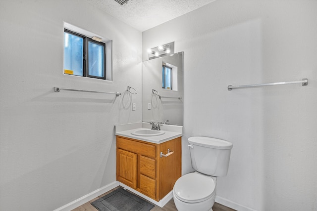 half bath featuring a textured ceiling, plenty of natural light, vanity, and toilet