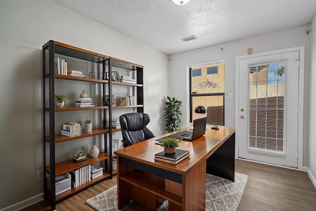 office area featuring baseboards, a textured ceiling, visible vents, and wood finished floors