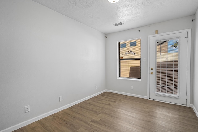 spare room featuring baseboards, a textured ceiling, visible vents, and wood finished floors