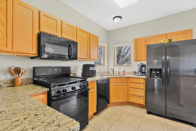 kitchen featuring light stone countertops, sink, light tile patterned floors, and black appliances