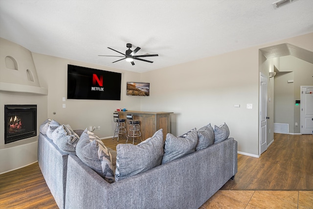 living room featuring dark wood-type flooring, a large fireplace, and ceiling fan