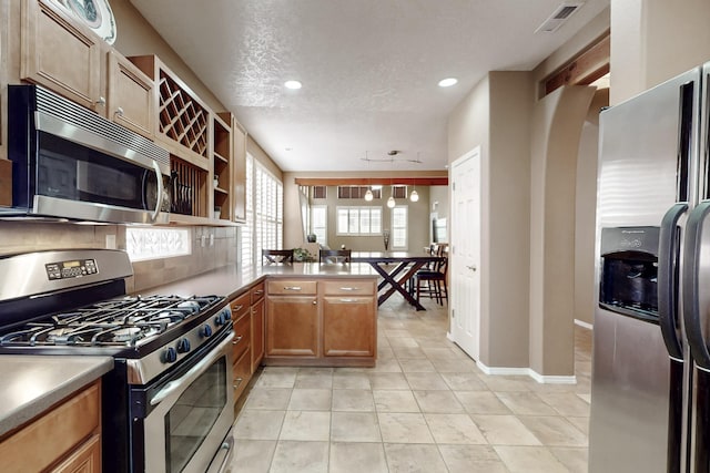 kitchen featuring decorative light fixtures, backsplash, kitchen peninsula, stainless steel appliances, and a textured ceiling