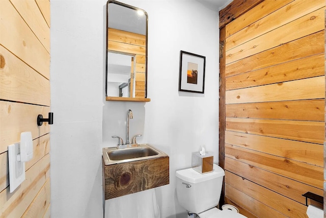 bathroom with sink, toilet, and wood walls