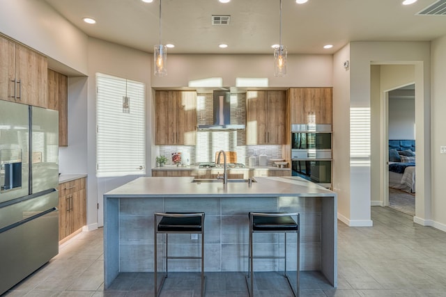 kitchen featuring appliances with stainless steel finishes, pendant lighting, a center island with sink, and wall chimney exhaust hood