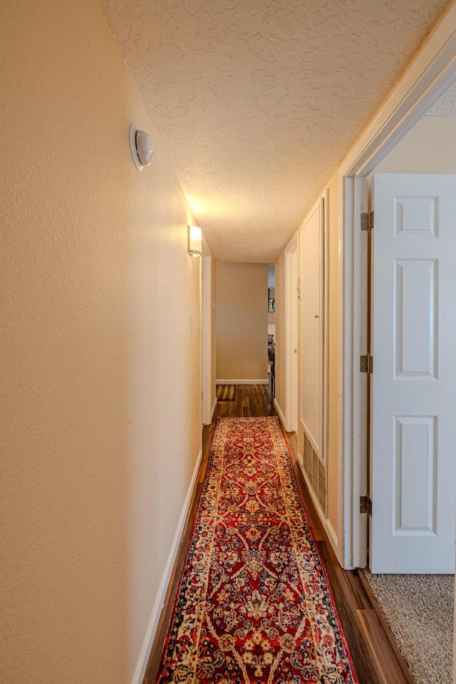 corridor with dark wood finished floors, a textured ceiling, and baseboards