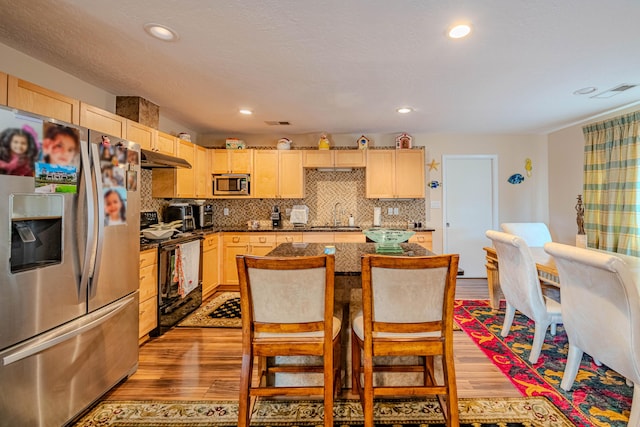 kitchen featuring light wood finished floors, stainless steel appliances, light brown cabinetry, and a kitchen island