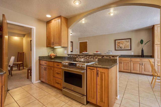 kitchen with dark stone countertops, light tile patterned floors, electric range, kitchen peninsula, and a textured ceiling