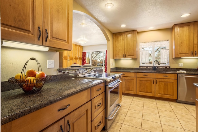 kitchen featuring sink, light tile patterned floors, stainless steel appliances, a textured ceiling, and dark stone counters