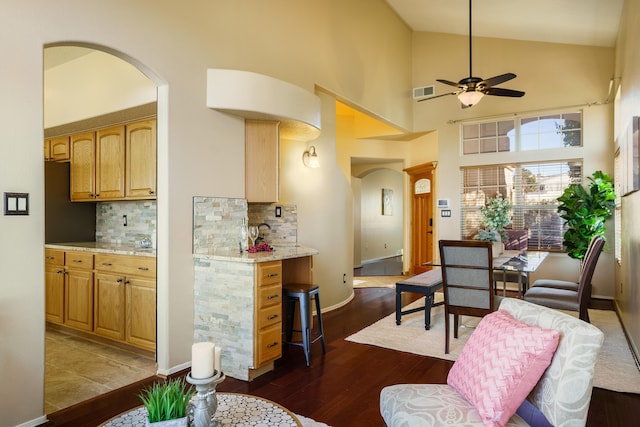 kitchen with dark hardwood / wood-style floors, high vaulted ceiling, tasteful backsplash, ceiling fan, and light stone countertops