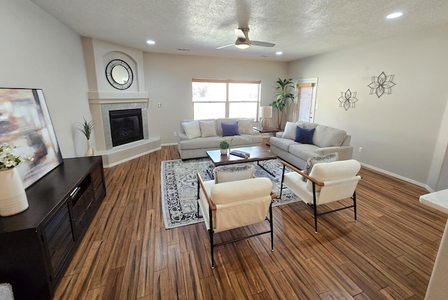 living room with dark wood finished floors, a textured ceiling, baseboards, and a tile fireplace