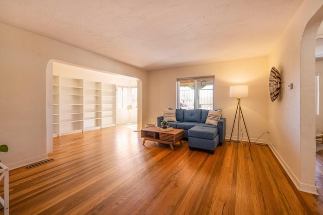 living area with arched walkways, visible vents, a textured ceiling, wood finished floors, and baseboards