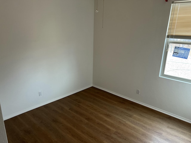 spare room featuring baseboards and dark wood finished floors