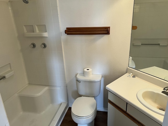 bathroom featuring a textured wall, toilet, vanity, baseboards, and walk in shower