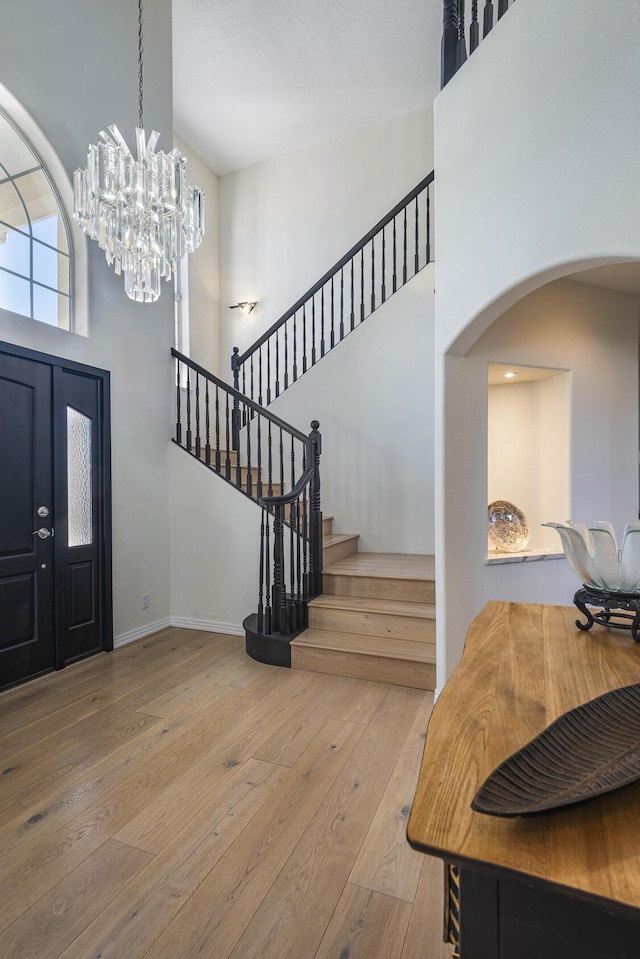 entryway featuring baseboards, arched walkways, stairway, wood finished floors, and a high ceiling