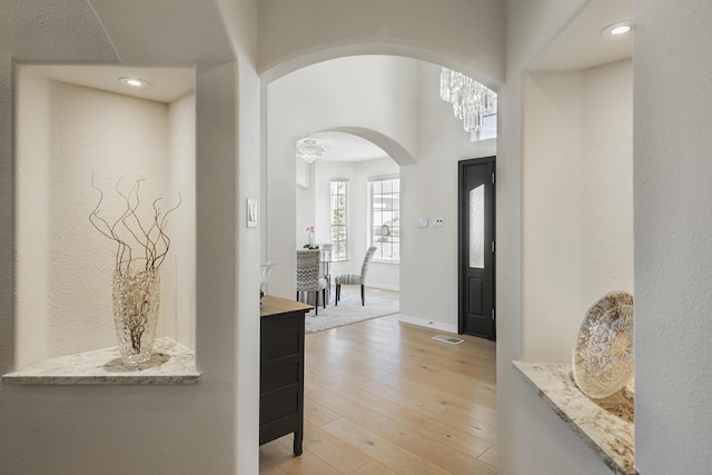 hall featuring light wood-style floors, arched walkways, and baseboards