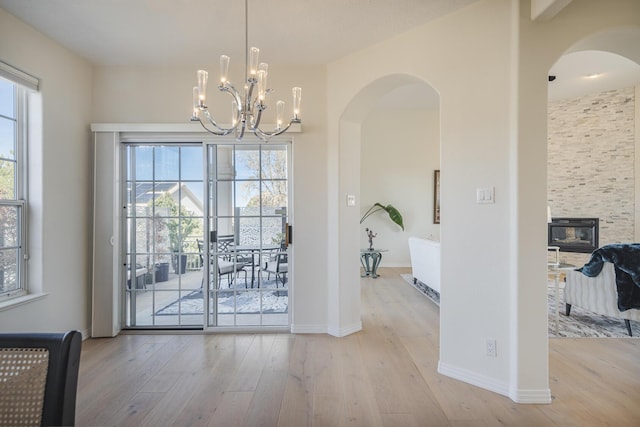 entryway with arched walkways, baseboards, a notable chandelier, and light wood finished floors