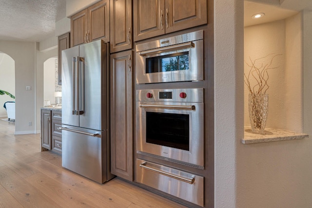 kitchen with a warming drawer, appliances with stainless steel finishes, arched walkways, and light stone countertops