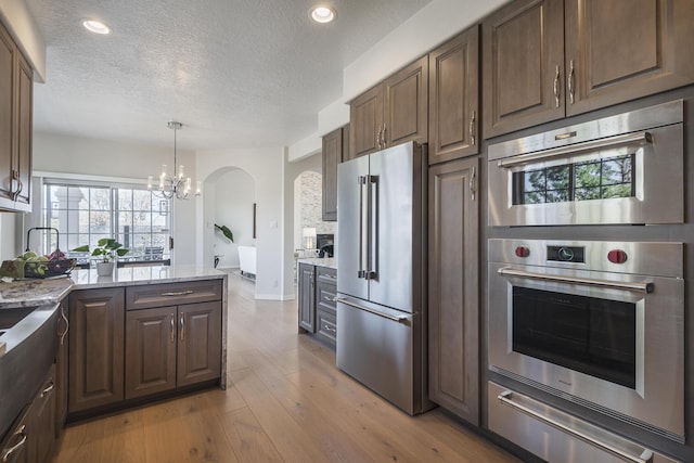 kitchen featuring a warming drawer, dark brown cabinetry, light stone countertops, light wood-type flooring, and high end refrigerator