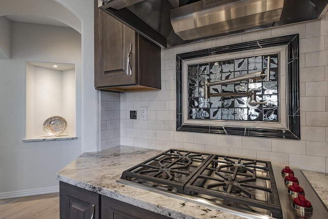 kitchen with dark brown cabinetry, tasteful backsplash, stainless steel gas stovetop, and light stone counters