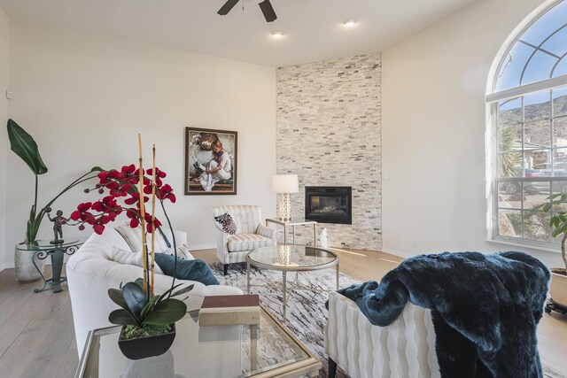 living area with ceiling fan, light wood-type flooring, a fireplace, and baseboards