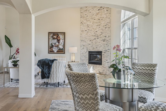 dining room featuring arched walkways, a large fireplace, baseboards, and light wood finished floors