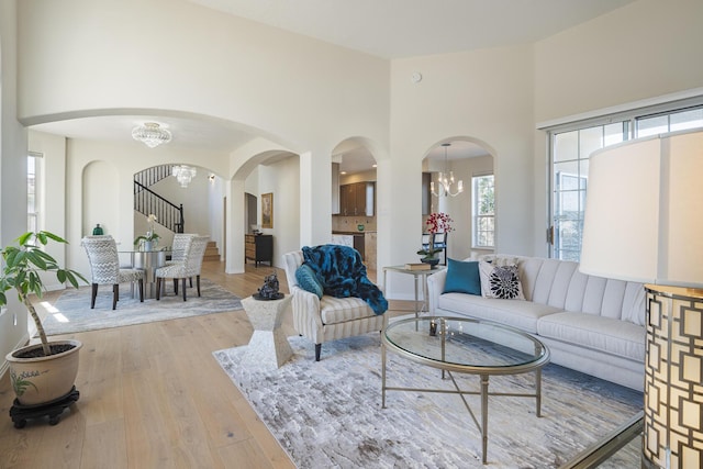 living area featuring arched walkways, stairway, a high ceiling, an inviting chandelier, and light wood-style floors