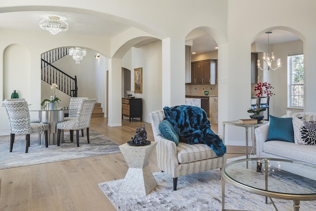 living area featuring stairs, light wood-type flooring, baseboards, and an inviting chandelier