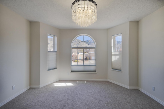 spare room featuring an inviting chandelier, visible vents, a wealth of natural light, and carpet flooring