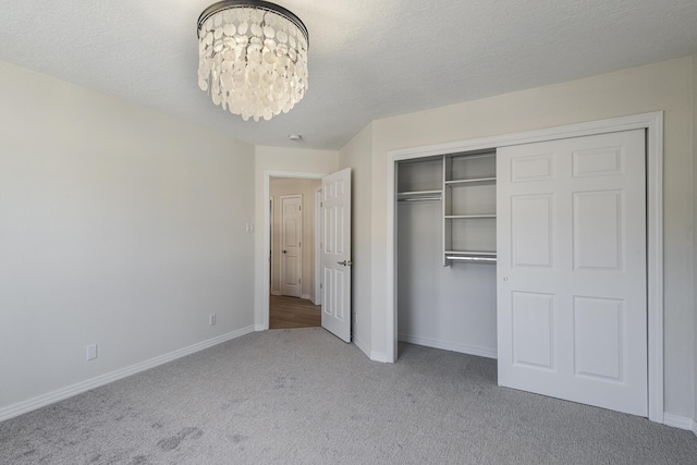 unfurnished bedroom with light carpet, baseboards, a textured ceiling, a chandelier, and a closet