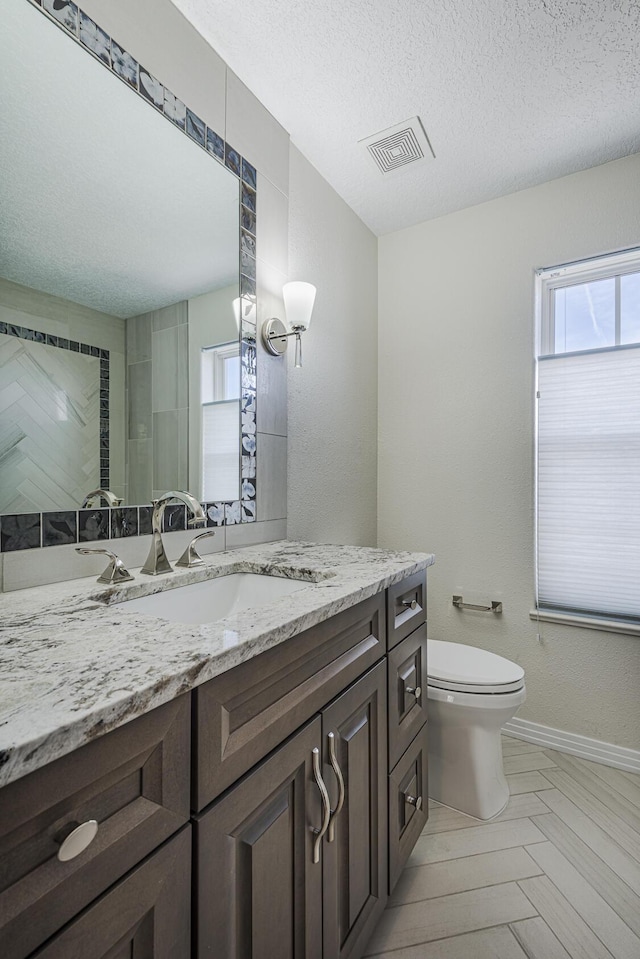 bathroom with a textured ceiling, toilet, vanity, visible vents, and baseboards