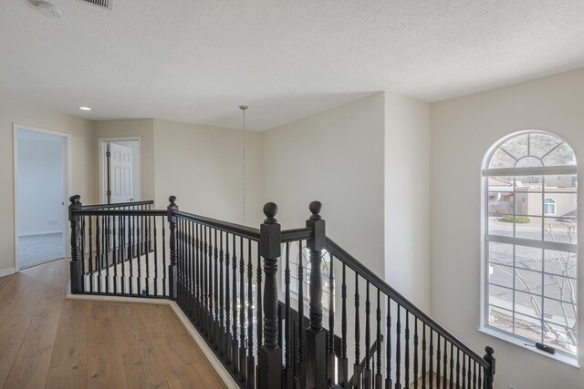 hall featuring a textured ceiling, wood finished floors, and an upstairs landing