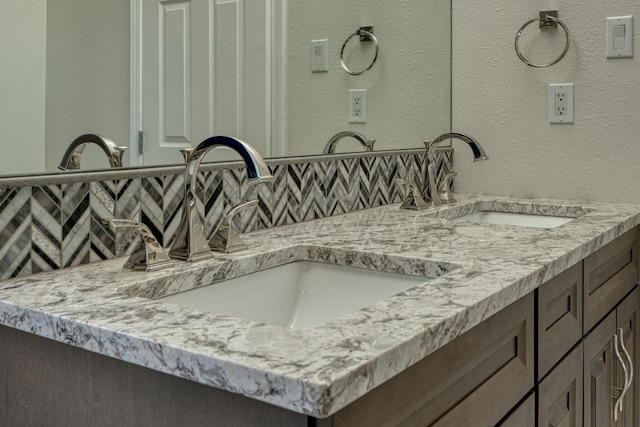 bathroom featuring double vanity, backsplash, a sink, and a textured wall