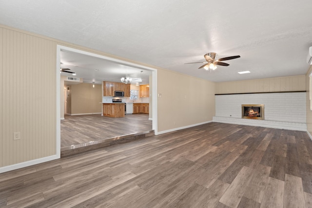 unfurnished living room with dark wood-style floors, a brick fireplace, baseboards, and ceiling fan with notable chandelier