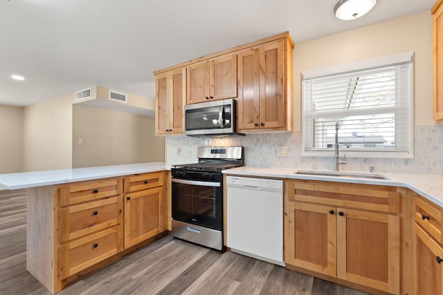 kitchen with visible vents, a peninsula, stainless steel appliances, light countertops, and a sink