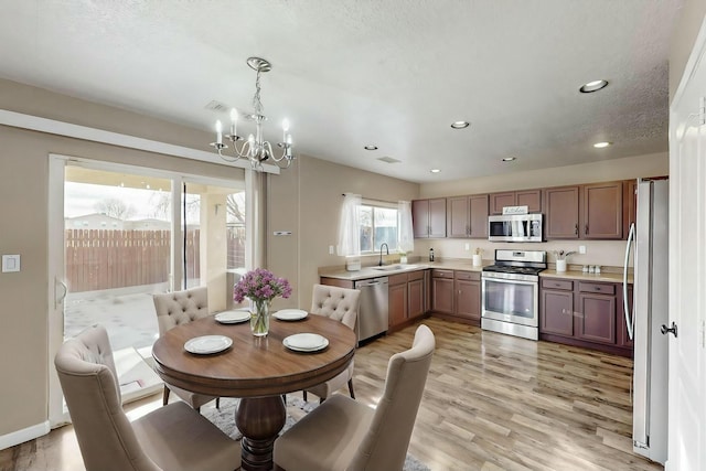 kitchen featuring sink, light wood-type flooring, stainless steel appliances, and decorative light fixtures