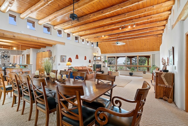 dining space with beam ceiling, wooden ceiling, a high ceiling, carpet flooring, and a warm lit fireplace