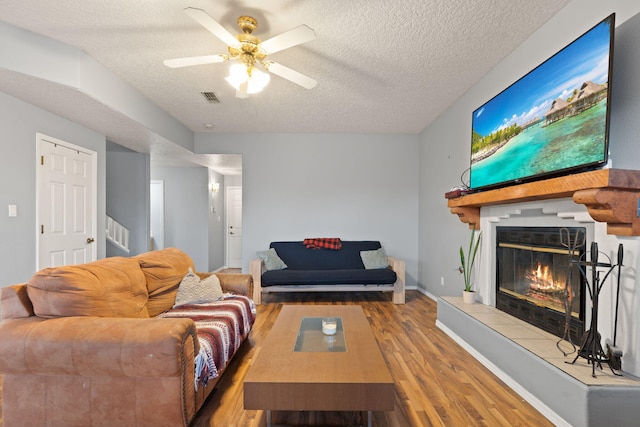 living room featuring a tiled fireplace, ceiling fan, hardwood / wood-style floors, and a textured ceiling