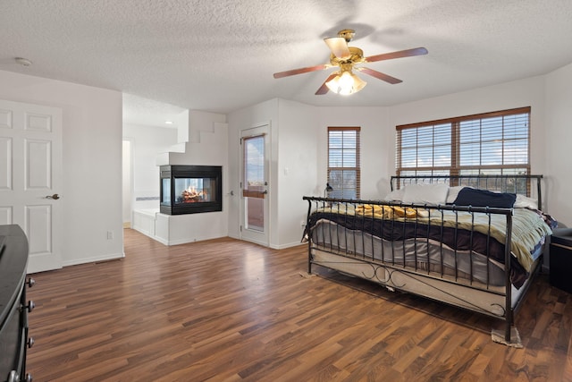 bedroom featuring ceiling fan, dark hardwood / wood-style floors, a textured ceiling, and a multi sided fireplace