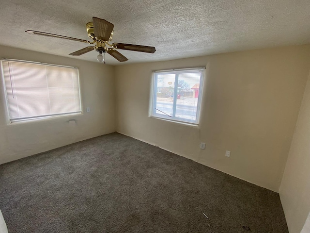 spare room featuring a textured ceiling, dark carpet, and a ceiling fan