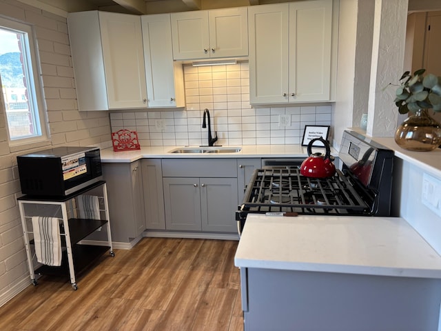 kitchen with sink, gas range, white cabinetry, light hardwood / wood-style flooring, and decorative backsplash