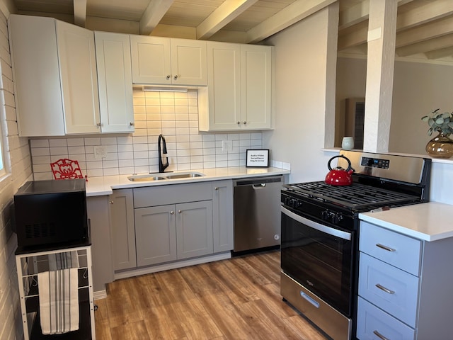 kitchen with stainless steel appliances, sink, white cabinets, and beam ceiling