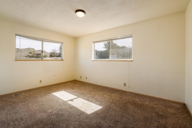 carpeted spare room featuring a textured ceiling, visible vents, and baseboards