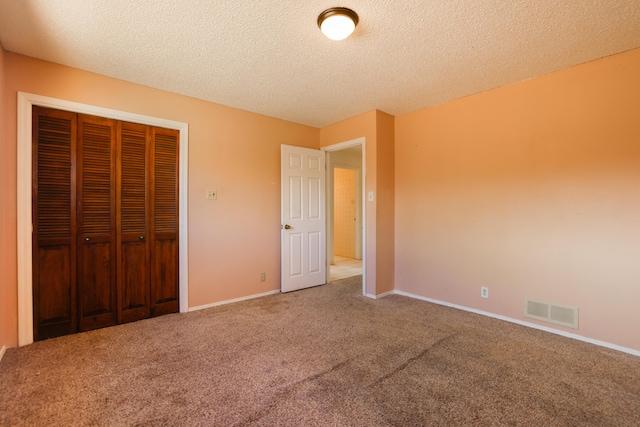 unfurnished bedroom with carpet floors, a textured ceiling, visible vents, and a closet