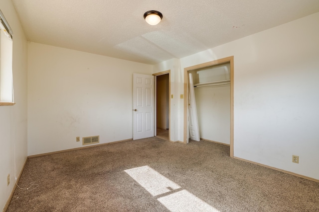 unfurnished bedroom with a textured ceiling, carpet flooring, visible vents, baseboards, and a closet