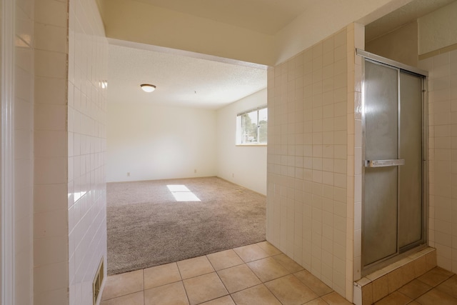 empty room featuring light carpet, light tile patterned floors, and a textured ceiling