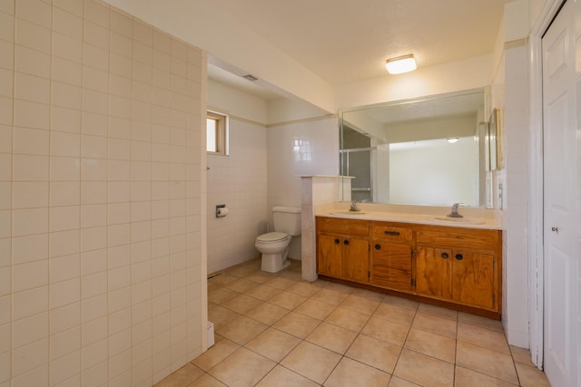 bathroom with a sink, double vanity, tile patterned flooring, and tile walls