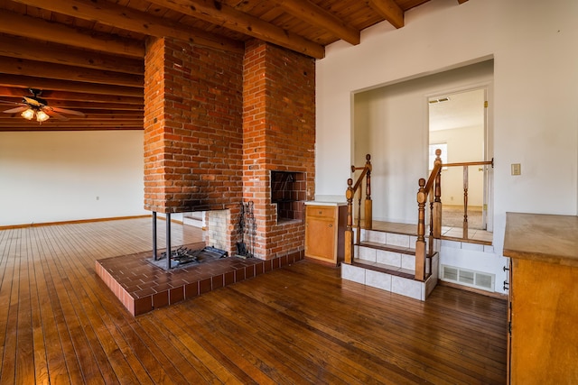 unfurnished living room featuring visible vents, dark wood finished floors, wooden ceiling, beamed ceiling, and a brick fireplace