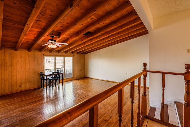 interior space with a ceiling fan, wood ceiling, wooden walls, wood finished floors, and beamed ceiling