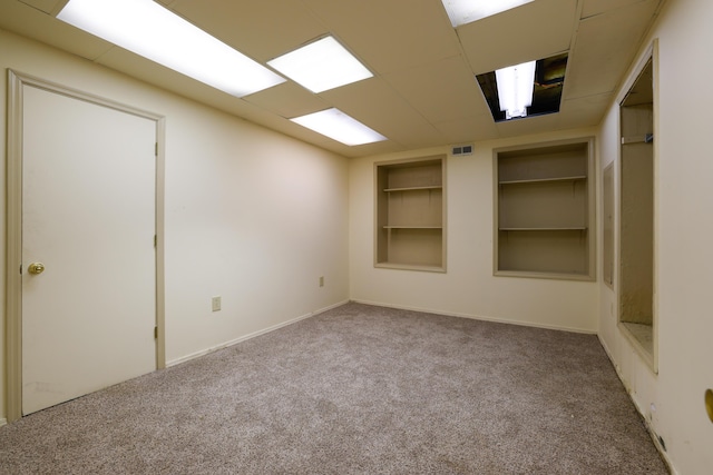 empty room with a paneled ceiling, built in shelves, visible vents, and carpet flooring